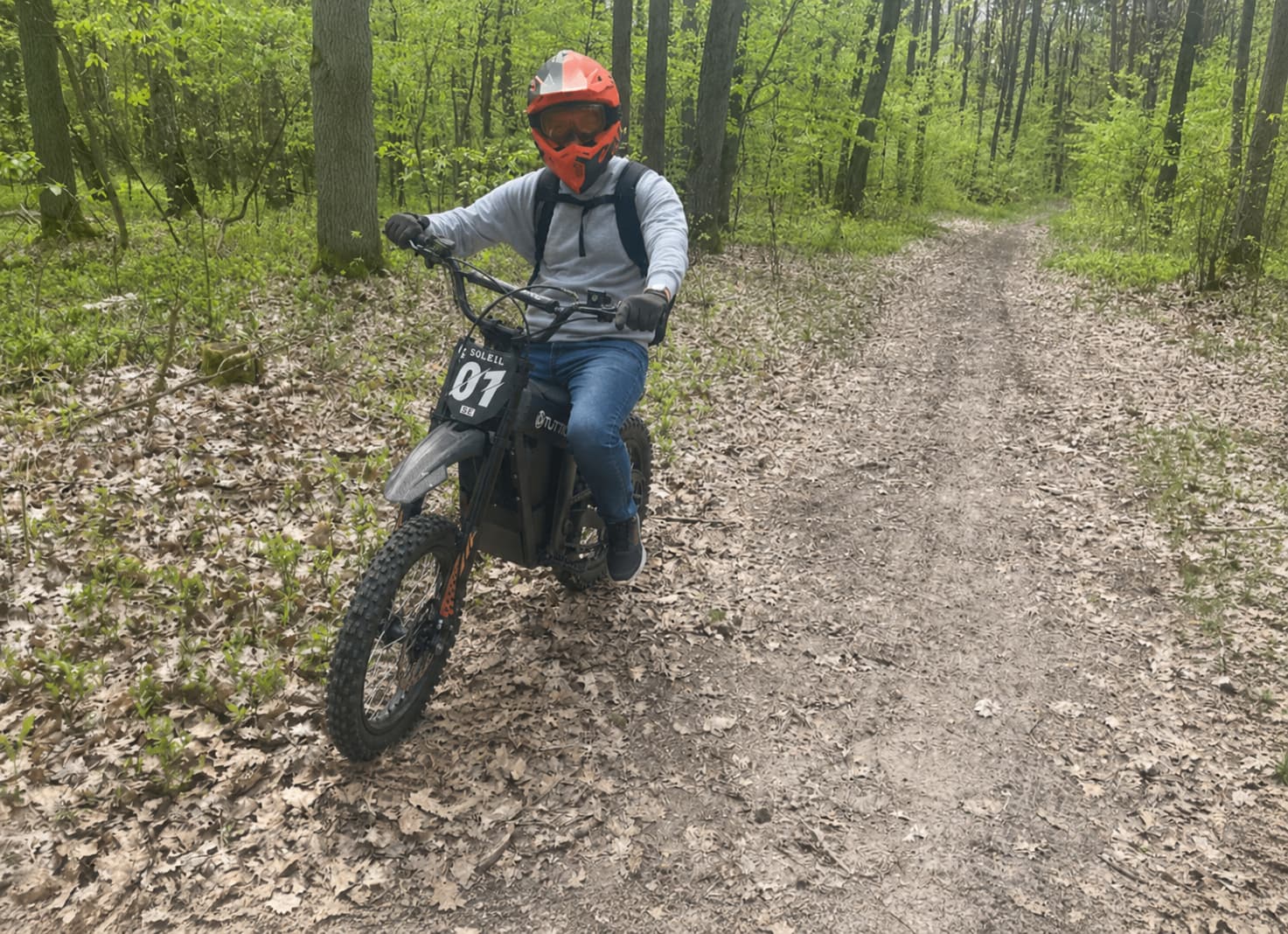 TUTTIO Soleil 01 SE electric dirt bike riding on a forest trail with an off-road rider in a natural outdoor scene.