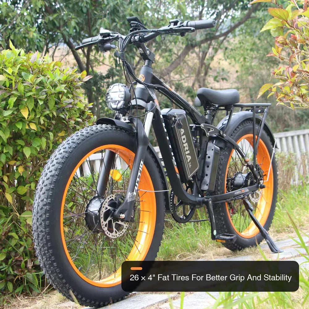 Low front side view of the Tuttio Adria26 outdoors, showing the black frame, orange rims, 26x4 fat tires, front headlight, rear rack, and fat tire grip and stability callout