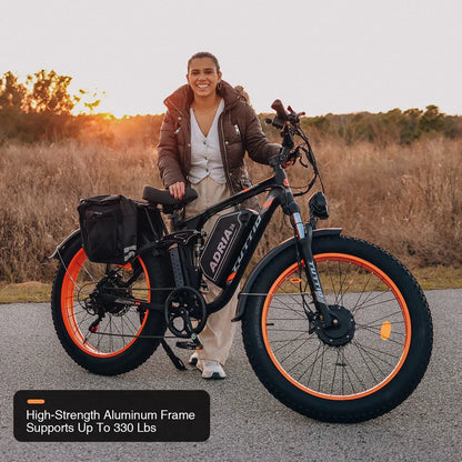 Smiling rider standing beside the Tuttio Adria26 at sunset, showing the black frame, orange rims, fat tires, rear side bag, front wheel stance, and aluminum frame strength callout