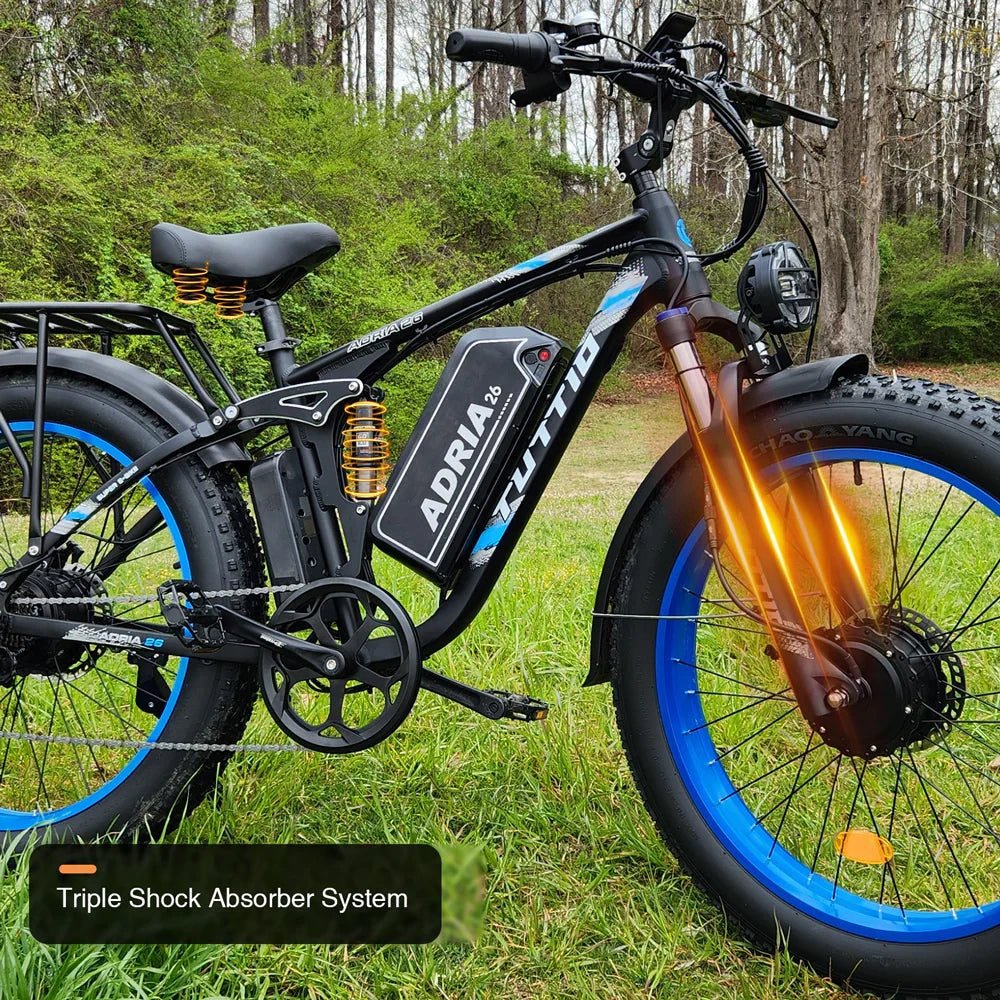 Close-up of the Tuttio Adria26 electric bike with blue rims parked on grass, featuring graphic overlays that highlight its triple shock absorber system including the front fork, rear frame, and seat springs.
